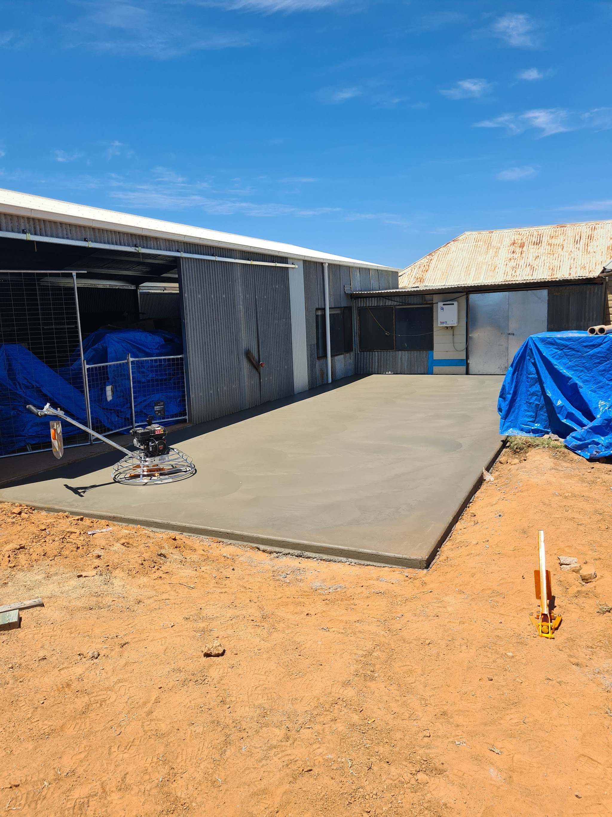 Freshly finished slab beside a shed with the power trowel still on the surface