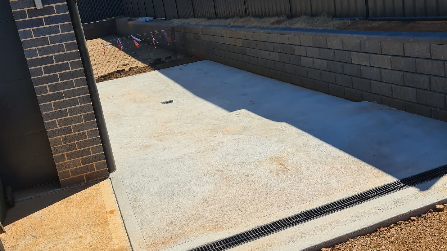 Broom-finished slab in a retaining-wall bay with a drainage grate